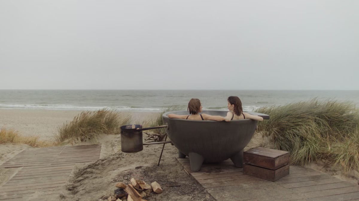 Two women enjoy a serene moment in a round bathtub by the ocean's edge.